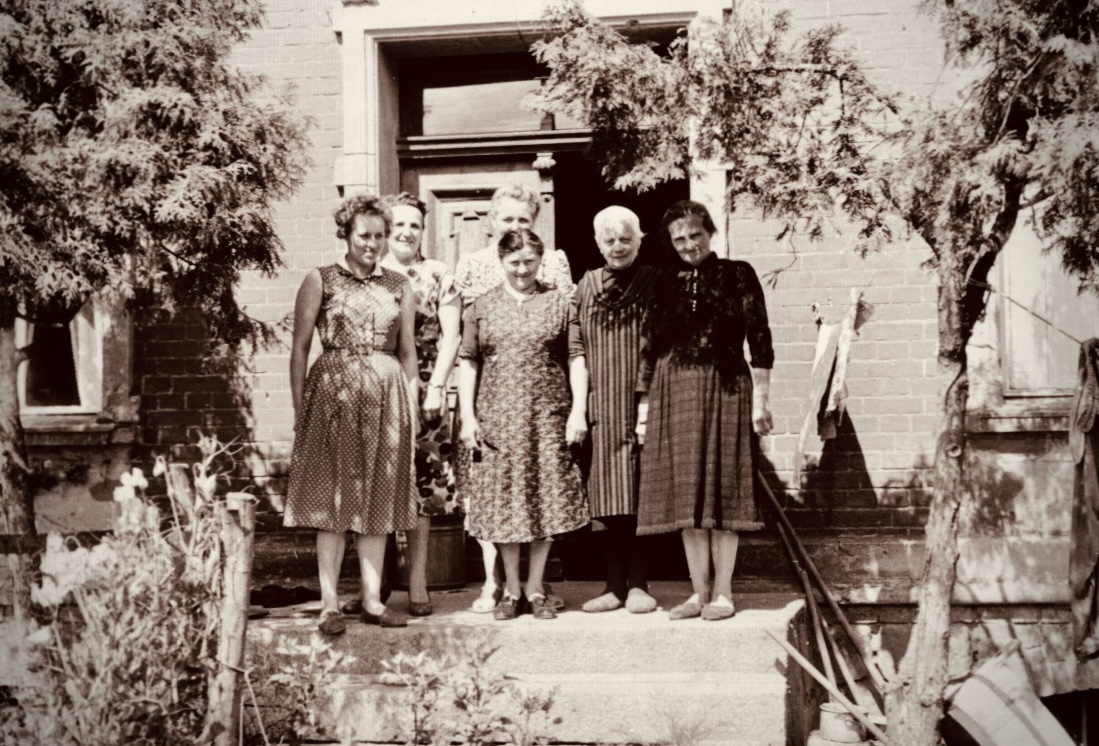 Es ist Sommer. Sechs Frauen stehen vor einem Haus.